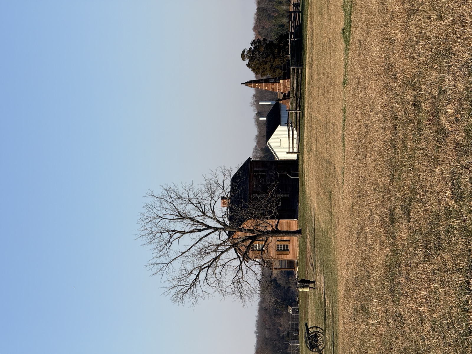 Historic farmhouse and cannon on a dry winter battlefield meadow under clear sky