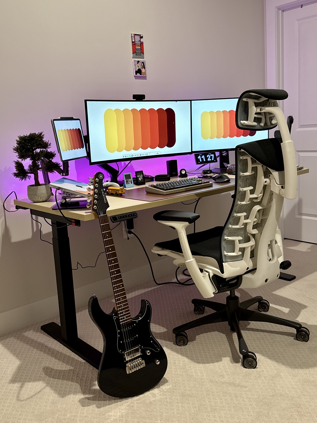 Home desk setup with dual monitors, ergonomic chair, and a black Yamaha Pacifica electric guitar