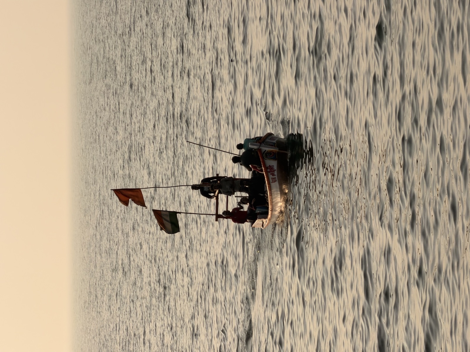 Fishing boat flying saffron and Indian flags on rippled water at sunset