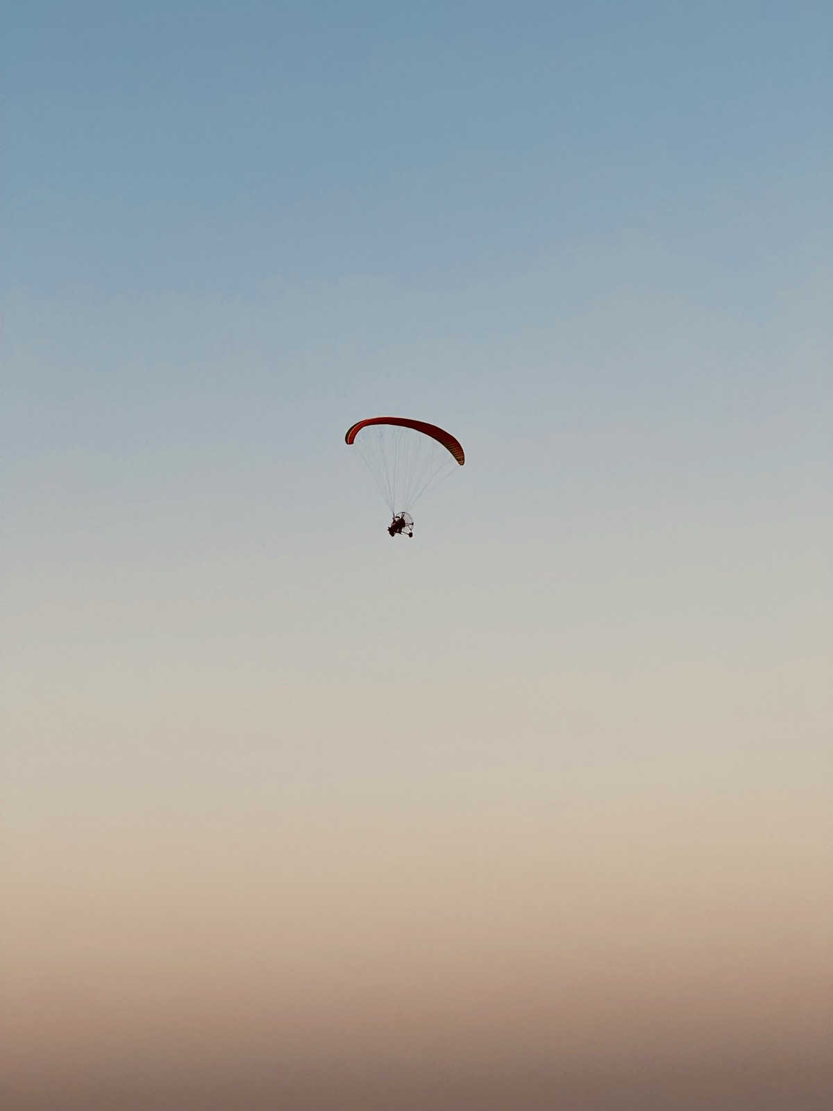 Powered paraglider drifting alone in a pastel dusk gradient sky