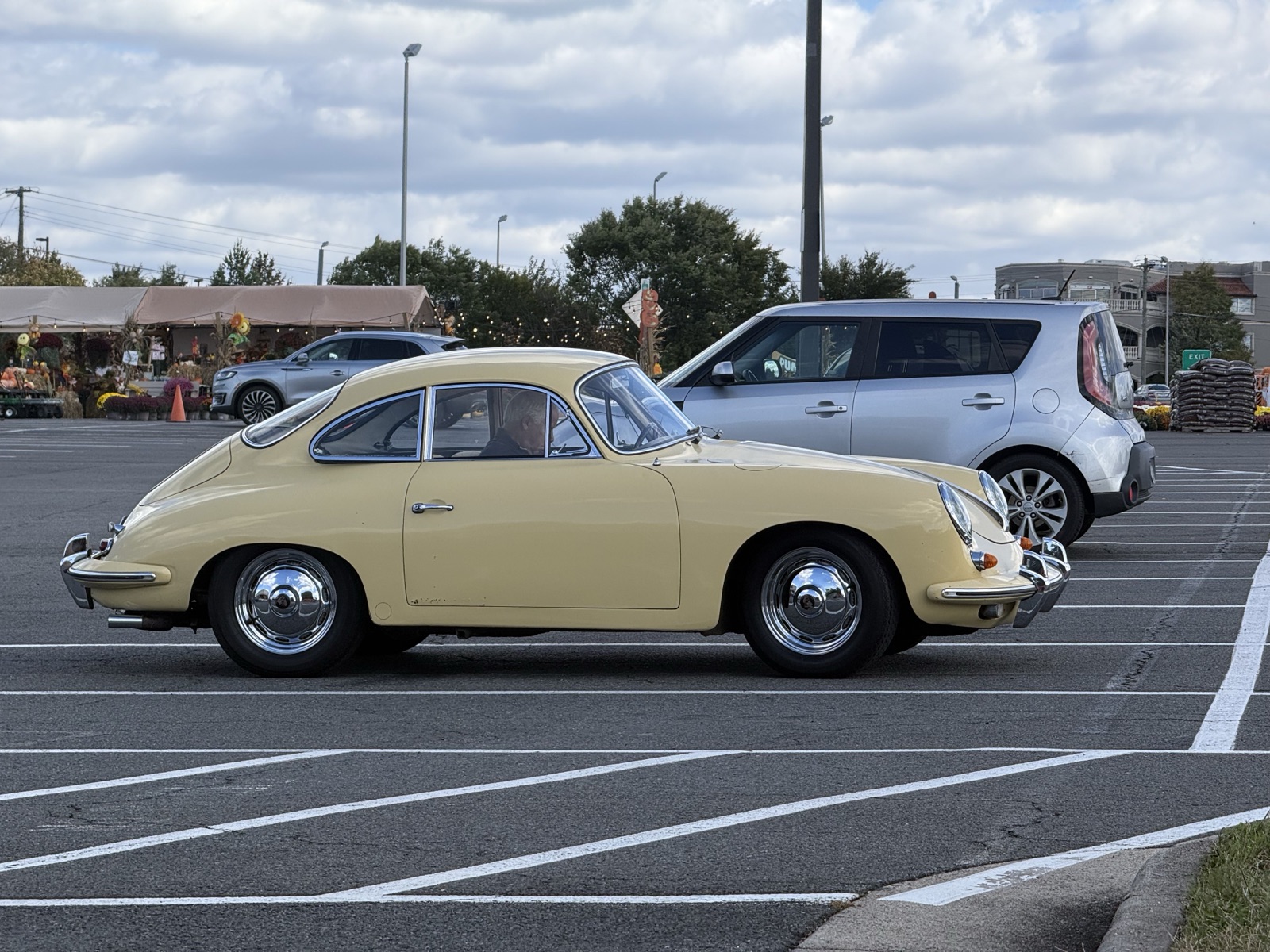 Pale yellow Porsche 356 coupe crossing a parking lot under overcast sky